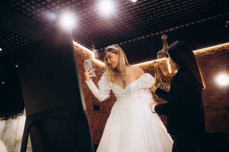 Téléchargez les photos : Une future mariée faisant du shopping pour une robe de mariée dans une boutique nuptiale. Photo de haute qualité - en image libre de droit