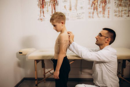 A pediatric neurologist doctor examines the back of a 5-year-old girl who has back pain. Treatment of muscle pain and scoliosis in children. High quality photo