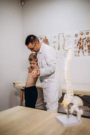 Ein Kinderneurologe untersucht den Rücken eines 5-jährigen Mädchens, das Rückenschmerzen hat. Behandlung von Muskelschmerzen und Skoliose bei Kindern. Hochwertiges Foto