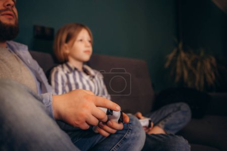 Excited by videogame victory little kid girl and her father raised hands scream with joy sit on sofa at home. Father his small daughter holds playing celebrate success feels happy. 