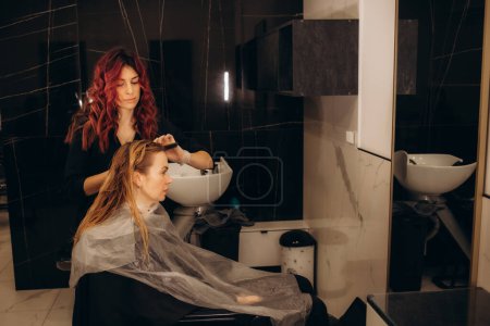 A female hairdresser dyes the hair of a young Caucasian woman with a brush and foil in a beauty salon. High quality photo