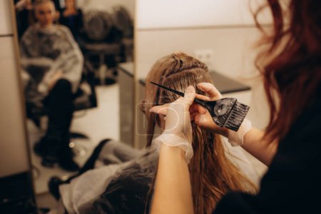 Hairdresser is applying bleaching powder on woman's hair and wrapping into the foil. . High quality photo