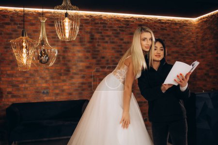 ein Berater in einem Hochzeitssalon zeigt einer Frau einen Katalog von Brautkleidern