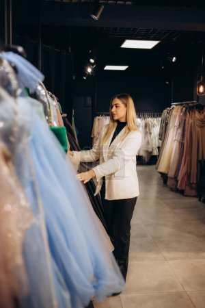 young beautiful woman chooses an evening dress in a store