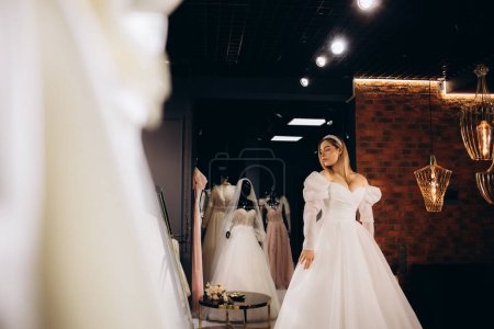 Téléchargez les photos : Une belle mariée essaie une robe de mariée dans un magasin - en image libre de droit