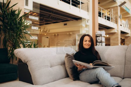 una mujer mira un catálogo de sofás mientras está sentada en una tienda de muebles