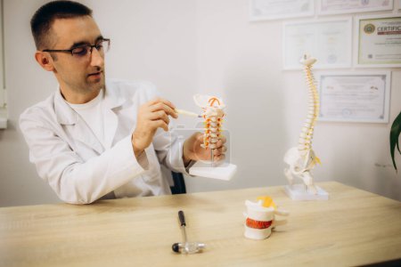 Foto de Médico masculino explicando anatomía espinal con modelo de columna vertebral al paciente en clínica. Foto de alta calidad - Imagen libre de derechos