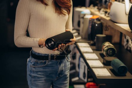 eine Frau in einem Elektronikgeschäft kauft einen tragbaren Lautsprecher