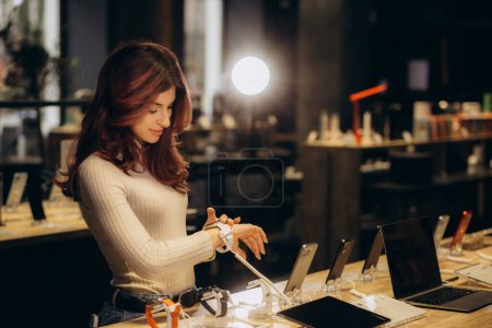 Comprando un nuevo dispositivo digital. Feliz hermosa mujer eligiendo un reloj inteligente en la tienda de tecnología. Foto de alta calidad