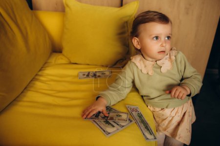little girl with dollars near the yellow sofa