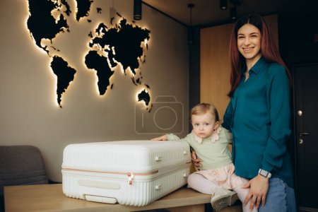 eine junge Mutter mit einer Tochter mit einem Koffer im Reisebüro