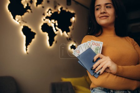 eine Frau hält einen Reisepass mit Geld vor dem Hintergrund einer hölzernen Weltkarte