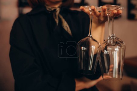Smiling female sommelier presenting a wine bottle with a blank label and a pair of glasses in a restaurant