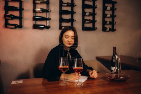 Brunette woman sommelier tasting smelling wine and writing notes.