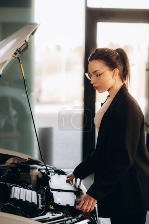 Téléchargez les photos : Une femme regarde sous le capot d'une voiture dans un concessionnaire automobile - en image libre de droit