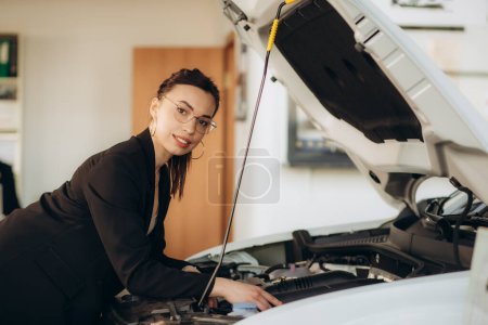 Téléchargez les photos : Une femme regarde sous le capot d'une voiture dans un concessionnaire automobile - en image libre de droit
