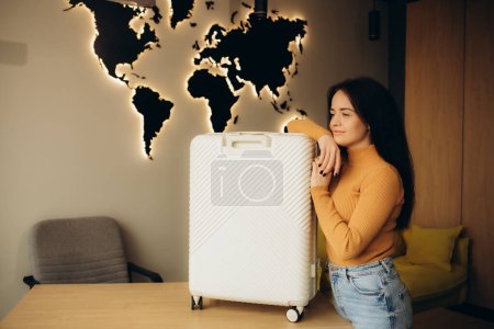 beautiful young woman with a suitcase in a travel agency on a background of a wooden world map