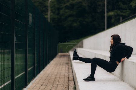 Mujer atlética haciendo empuje inverso hacia arriba en escaleras fitness al aire libre.