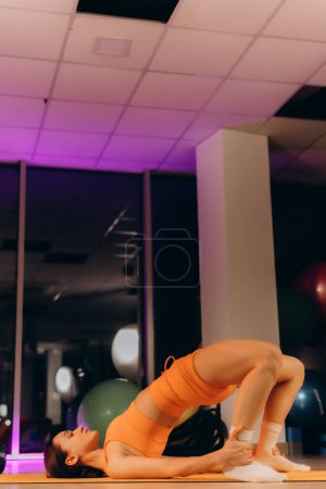 an athletic woman in an orange suit stretches in the gym