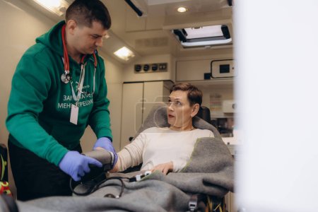 A doctor takes the blood pressure of an older woman in an ambulance