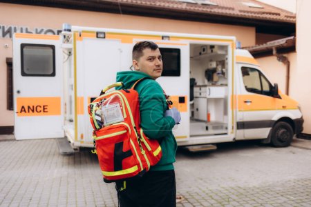 Téléchargez les photos : Masculin ambulancier posant pour caméra, ambulance en arrière-plan, professionnalisme - en image libre de droit