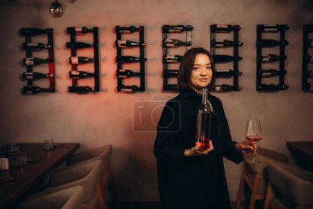 Female sommelier swirling red wine in glass on cellar background being in cellar. Wine expert exam to study different wine. 