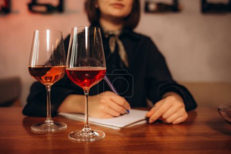 Extremo acercamiento de la mano femenina tomando notas en la cata de vinos tintos
.