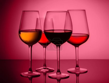 Foto de Set de cuatro copas de vino con vino tinto, blanco y rosa sobre fondo viva magenta - Imagen libre de derechos
