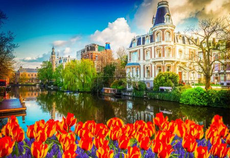 Foto de Paisaje con uno de los canales en el casco antiguo de Amsterdam con tulipanes, Países Bajos, tonificado - Imagen libre de derechos