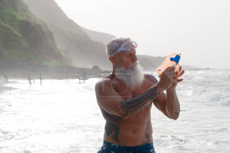 Glücklich fitter Senior, der mit Wasserpistole Spaß im Meer hat. Ältere gesunde Menschen Lebensstil und sportliche Betätigung