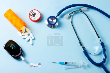 White pills in orange bottle with blood glucose meter ans stethoscope on blue background with copy space