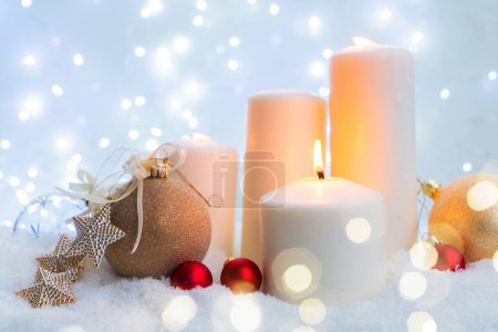 Téléchargez les photos : Noël blanc - bougies incandescentes de l'Avent dans la neige blanche, nuit bleue avec lumières en arrière-plan - en image libre de droit