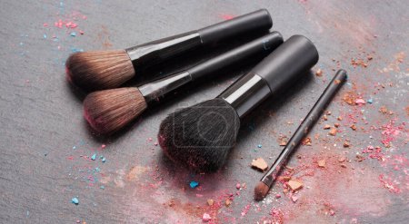 Téléchargez les photos : Ensemble de pinceaux de maquillage avec des crumbles de maquillage sur fond noir - en image libre de droit