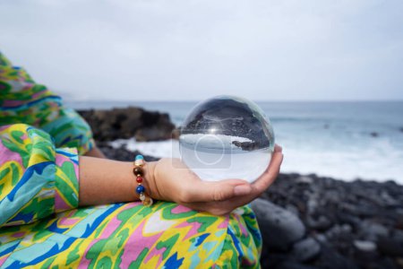 Frau meditiert am wilden Strand und hält Kristallkugel in der Hand