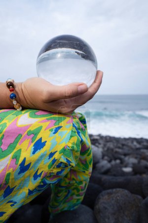 Frau meditiert am wilden Strand und hält Kristallkugel in der Hand