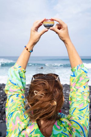 Frau meditiert am wilden Strand und hält Kristallherz