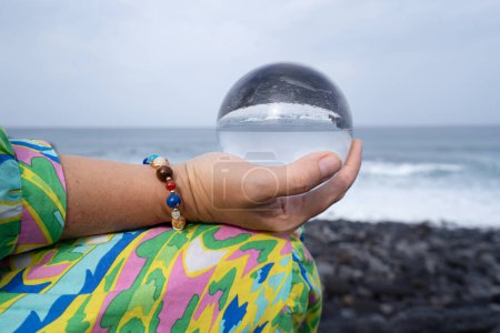 woman meditating on wild beach shore and holding crystal ball