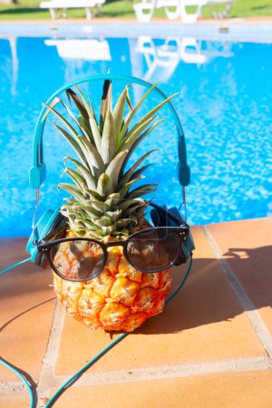 pinapple near swimming pool in sunglasses and headphones