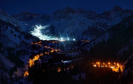 Landscape of glowing road from Medeu ice skate to Shymbulak ski resort at Tian Shan mountains at night time in Almaty city, Kazakhstan
