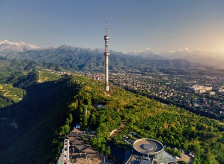 Drohnenaufnahmen vom hohen Fernsehturm der Stadt Almaty und dem Park auf dem Koktobe-Hügel vor Schneebergen in Kasachstan