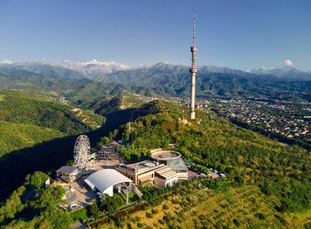 Aerial drone shot of Koktobe hill park with Ferris wheel an symbol Almaty city high TV tower against snow mountains in Kazakhstan