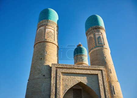Téléchargez les photos : Vieille madrasah mineure avec quatre tours minaret et nid de cigogne au sommet au centre de la ville de Boukhara en Ouzbékistan - en image libre de droit