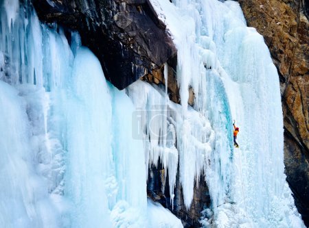 Luftaufnahme eines Athleten in orangefarbener Jacke Eisklettern am großen gefrorenen Wasserfall in der Barskoon-Schlucht im Gebirgstal in Kirgisistan