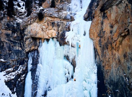 Aerial drone view of athlete Ice climbing big frozen waterfall in Barskoon gorge the mountain valley in south part of Issyk Kul lake, Kyrgyzstan