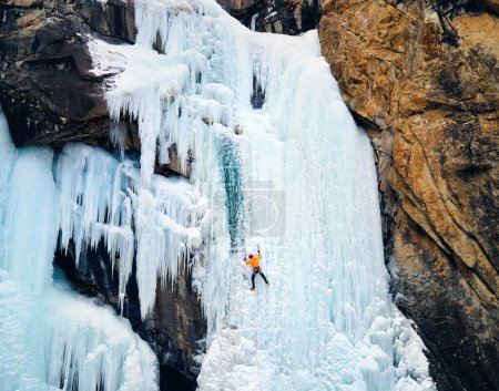 Luftaufnahme eines Athleten in orangefarbener Jacke Eisklettern am großen gefrorenen Wasserfall in der Barskoon-Schlucht im Gebirgstal in Kirgisistan