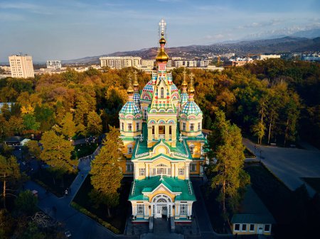 Téléchargez les photos : Vue aérienne par drone de l'église orthodoxe russe de la cathédrale de l'Ascension et des montagnes de neige en arrière-plan dans le parc Panfilov contre le ciel couchant dans la ville d'Almaty, Kazakhstan - en image libre de droit