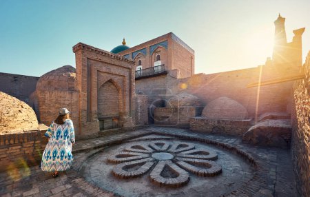 Woman tourist in ethnic dress at Inner Yard with floor in flower shape from stones near madrasah at ancient city wall at Khiva in Uzbekistan. 