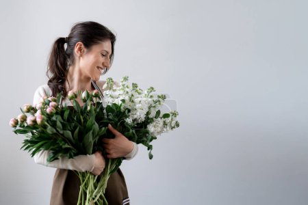 WOMAN florist EMBRACING a bunch of white and pink flowers on white background indoors