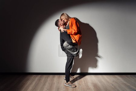 Téléchargez les photos : Un moment ludique, un homme soulève une femme dans une étreinte spontanée et joyeuse, leurs ombres dansant sur le mur - en image libre de droit