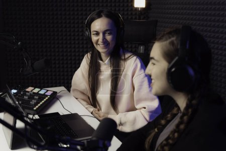 Photo for Two happy podcast hosts share a light-hearted moment, laughing together during a podcast recording in a soundproof studio - Royalty Free Image
